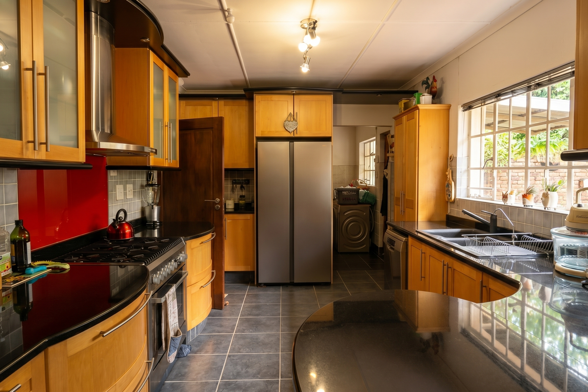 A functional kitchen featuring light wood cabinetry, black granite countertops, a gas stove with extractor fan, and tiled flooring with a view to the rear.