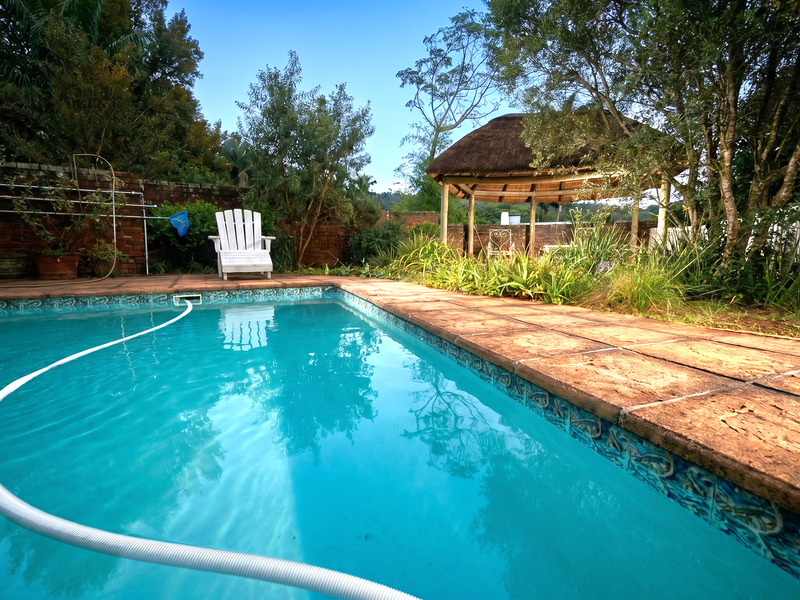 Outdoor pool area featuring a swimming pool, paved surround, and a thatched gazebo set within a private garden with brick boundary walls.