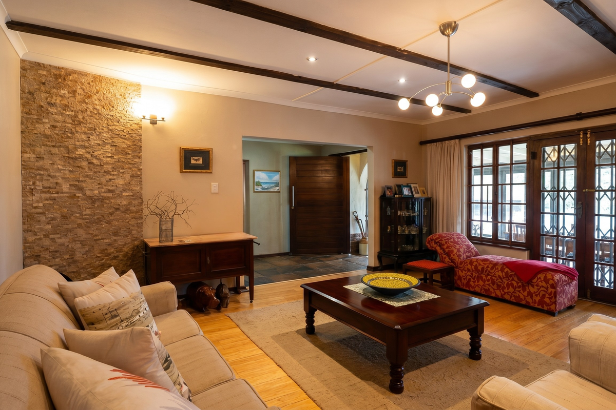 A well-maintained living room featuring exposed timber ceiling beams, a textured stone feature wall, hardwood flooring, and direct access to an outdoor area.