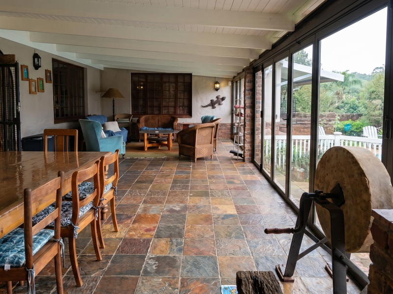 Spacious covered patio featuring slate tile flooring, exposed beam ceiling, and large sliding glass doors overlooking the pool area.