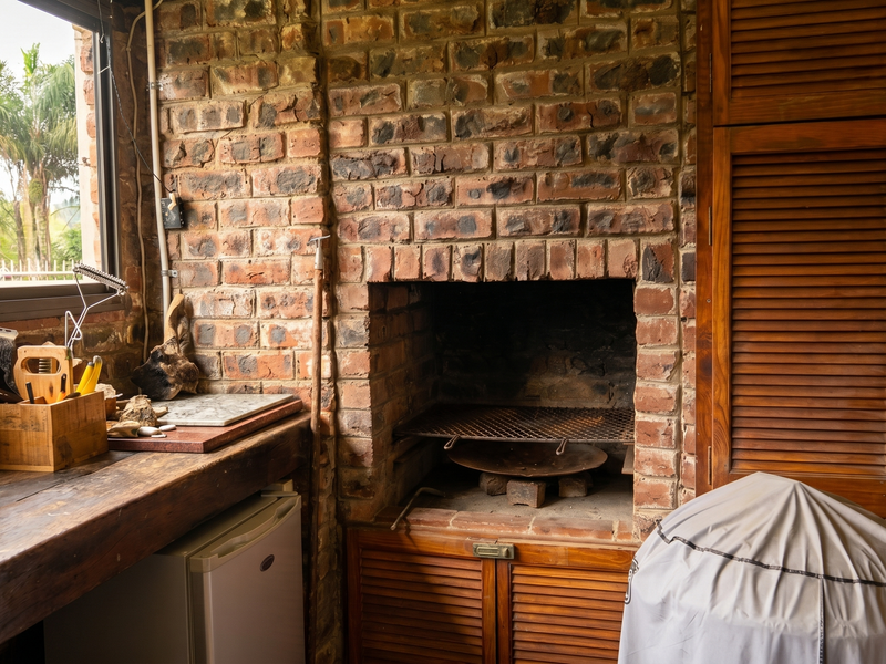 An indoor braai area featuring a rustic brick fireplace, wooden cabinetry, and a solid timber countertop, perfect for entertaining.