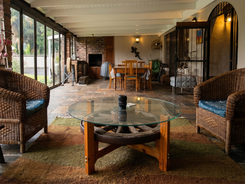 Spacious covered patio featuring tiled flooring, exposed beam ceiling, and a built-in braai, enclosed by large sliding glass doors for seamless indoor-outdoor living.