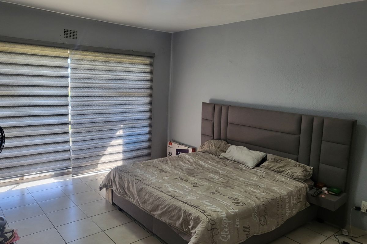 A spacious bedroom featuring tiled flooring, a large sliding glass door with modern zebra blinds, and a built-in ventilation grille.