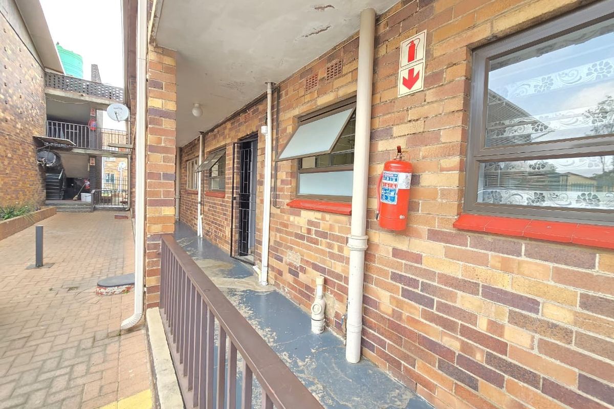 Exterior walkway of a townhouse complex featuring face brick walls, metal railings, and functional fire safety equipment.