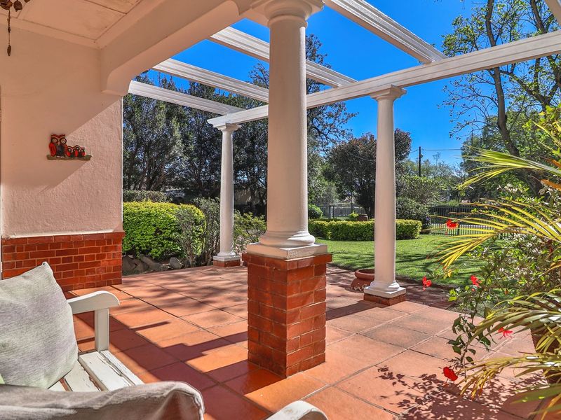 A covered patio featuring a pergola structure, brick columns, and terracotta tiling, overlooking a well-maintained garden.