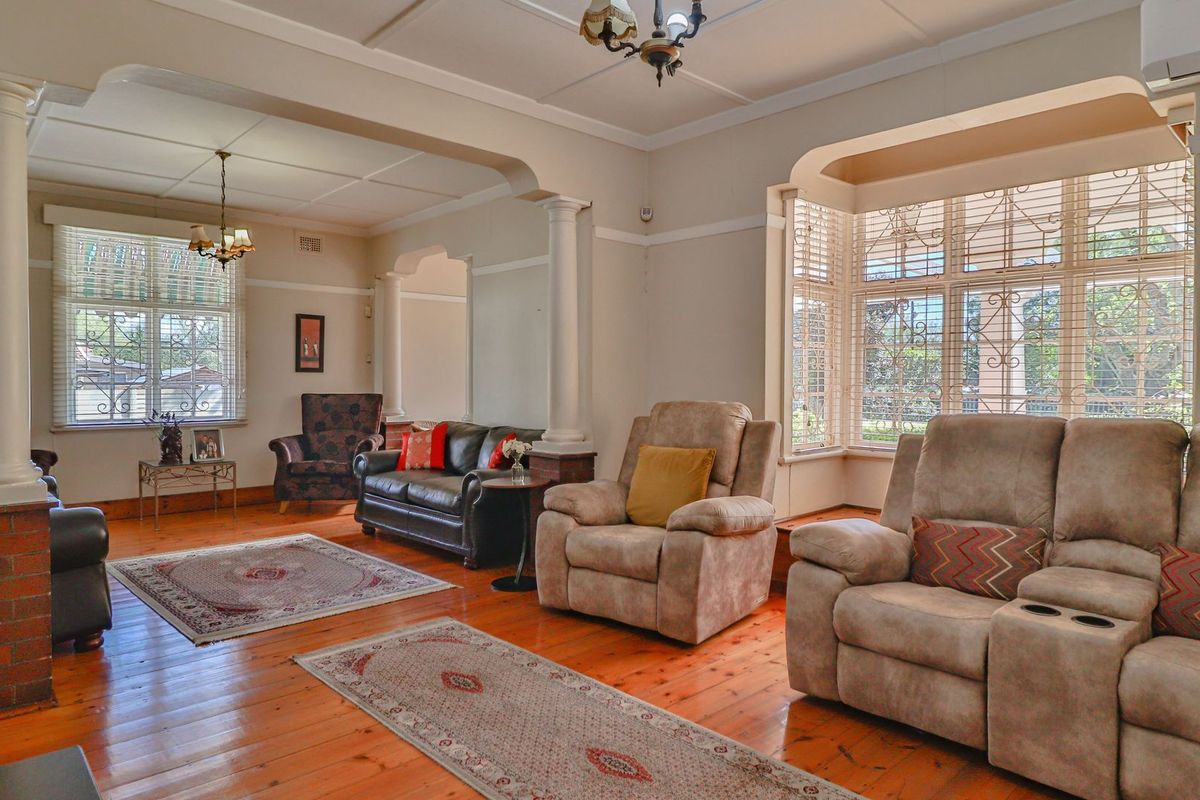 Spacious living room featuring polished hardwood floors, classic decorative columns, an elegant archway, and a large bay window providing ample natural light.