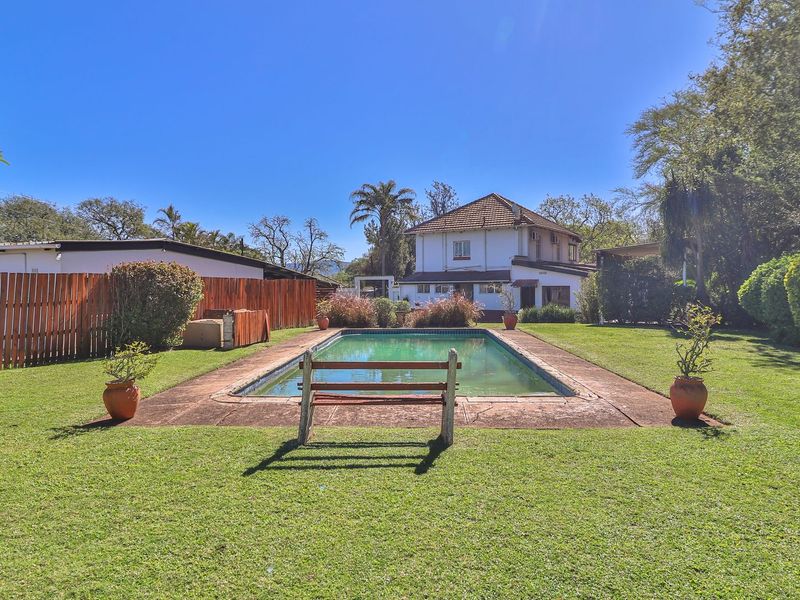 Spacious rear garden featuring a swimming pool with paved surround, enclosed by timber fencing and mature landscaping.