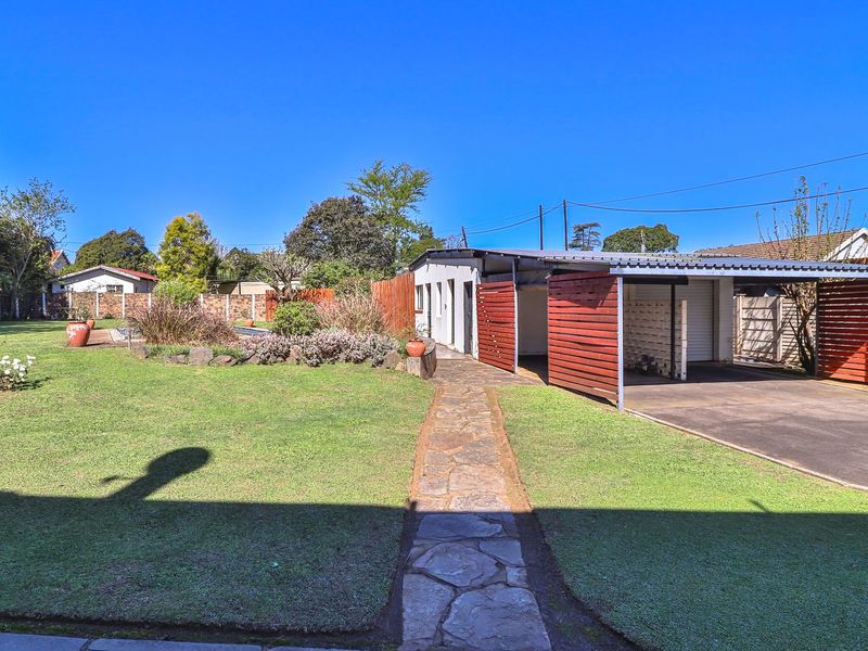 A spacious rear garden featuring a stone pathway leading to a covered carport and established landscaping with timber boundary fencing.