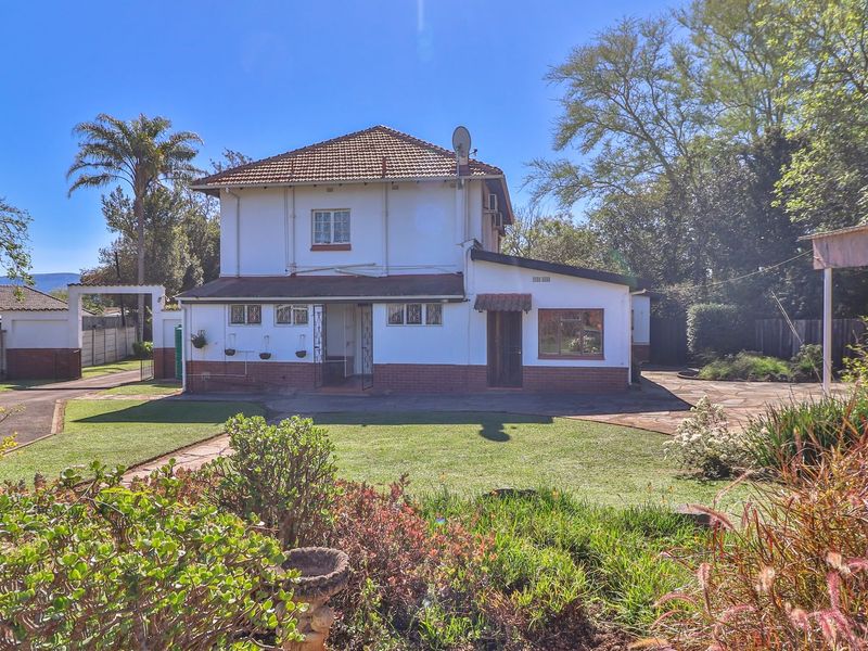 Rear view of a two-story residential house featuring a tiled roof, paved driveway, and established garden area.