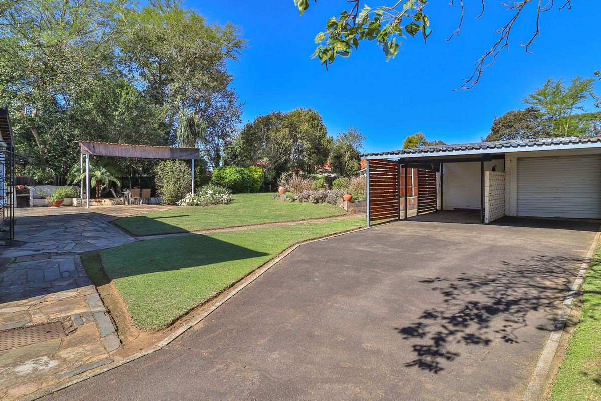 Spacious rear garden featuring a paved driveway, a covered carport with timber screening, a stone patio area, and a pergola.