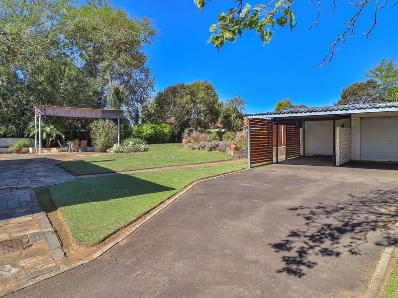 Spacious rear garden featuring a paved driveway, a covered carport with timber screening, a stone patio area, and a pergola.
