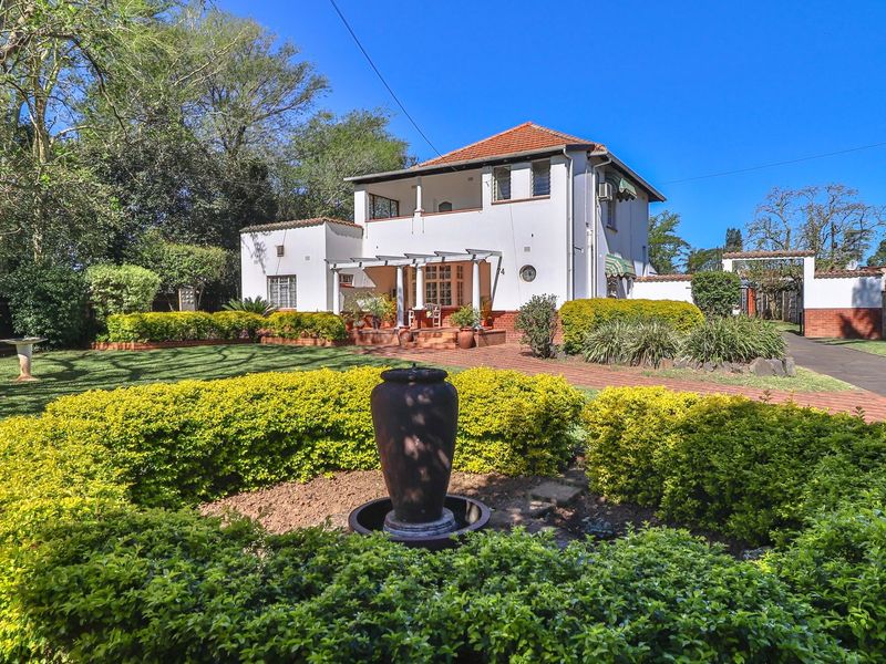 A well-maintained two-story residence featuring a classic terracotta roof, a covered patio area, and a beautifully landscaped front garden with a central water feature.