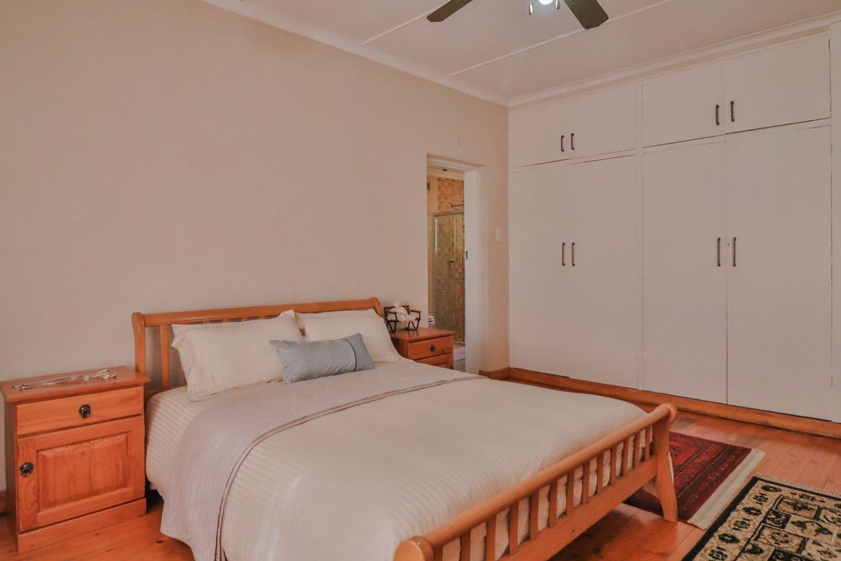 A bedroom featuring timber flooring, built-in cupboards, and a ceiling fan, with an adjoining en-suite bathroom visible.