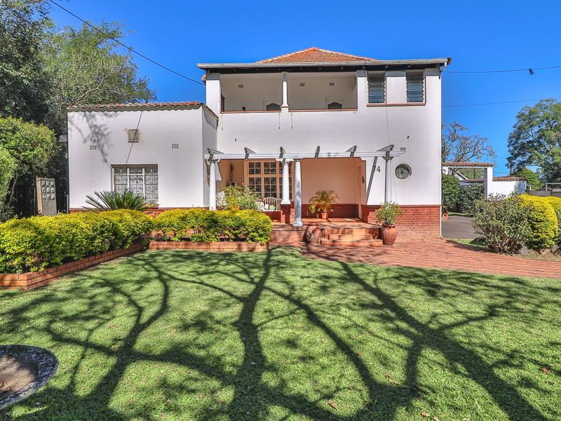 A charming double-story house featuring a covered patio, balcony, and well-maintained front garden with brick-paved driveway and entrance.