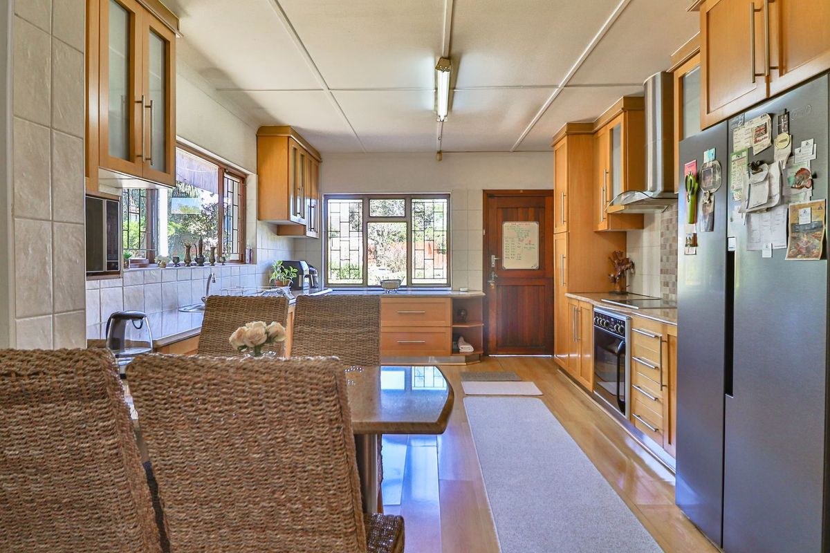 A functional kitchen featuring wooden cabinetry, built-in oven, stainless steel extractor fan, and tiled backsplash with ample natural light.