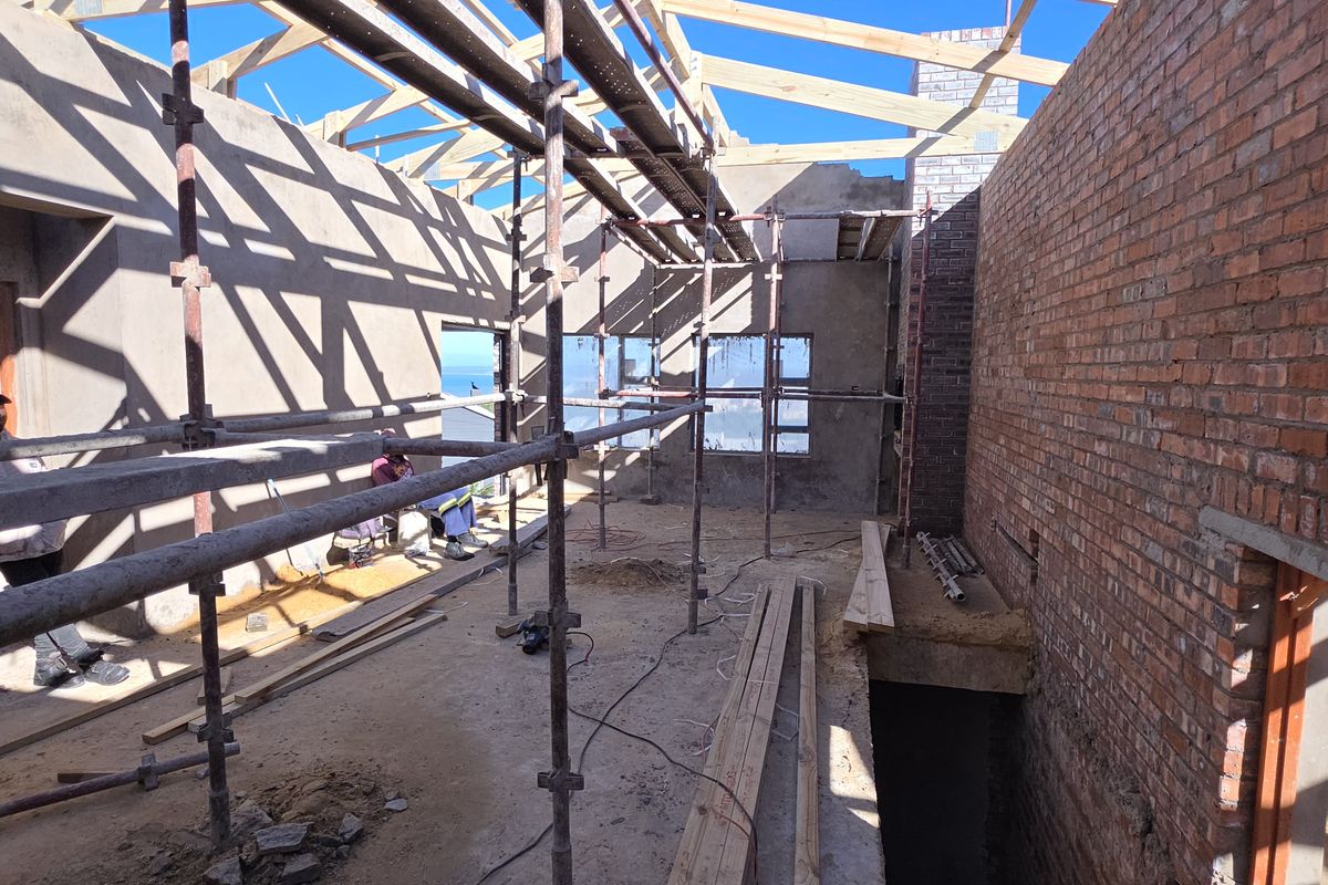 An interior view of a property under construction, featuring exposed brick walls, open roof trusses, and scaffolding throughout the space.