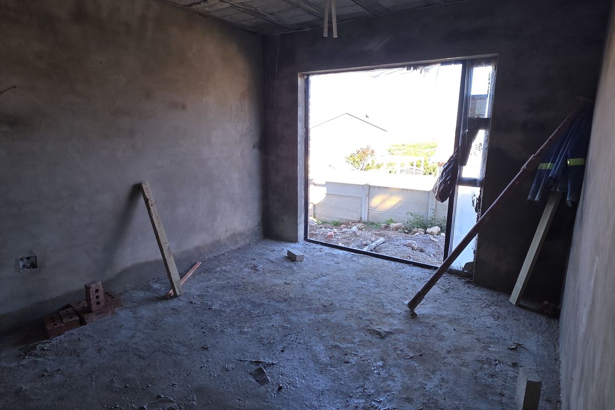 An unfinished bedroom interior in shell condition, featuring raw plaster walls, exposed concrete flooring, and a large window opening.
