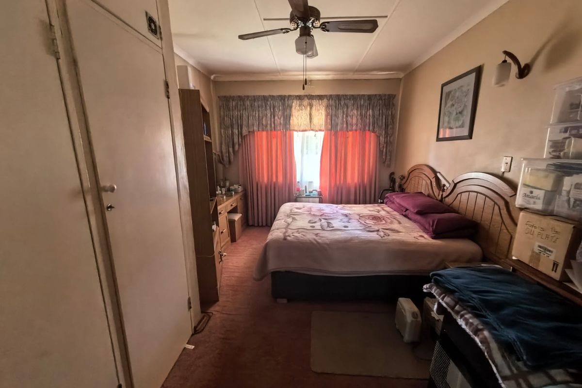 A bedroom featuring a ceiling fan, built-in cupboard storage, and carpeted flooring, offering a functional space with potential for cosmetic updates.