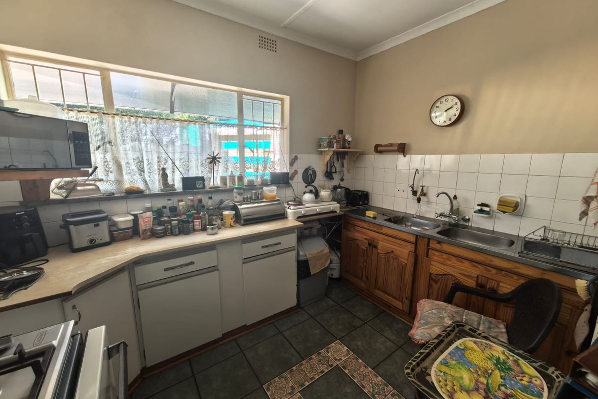 A functional kitchen featuring timber cabinetry, double sink, laminate countertops, and tiled splashbacks, offering potential for a modern renovation.