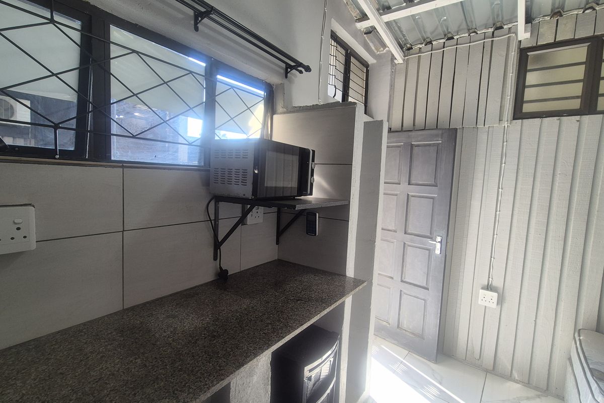 A functional scullery or utility area featuring a granite countertop, tiled splashback, and security bars on the windows.