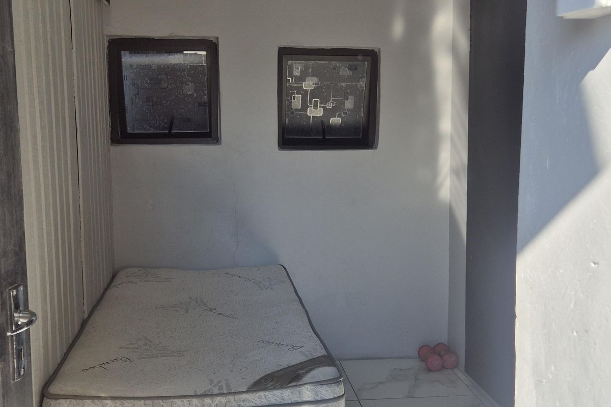 A compact bedroom featuring tiled flooring and exposed roof rafters, providing a basic functional space with potential for cosmetic improvement.