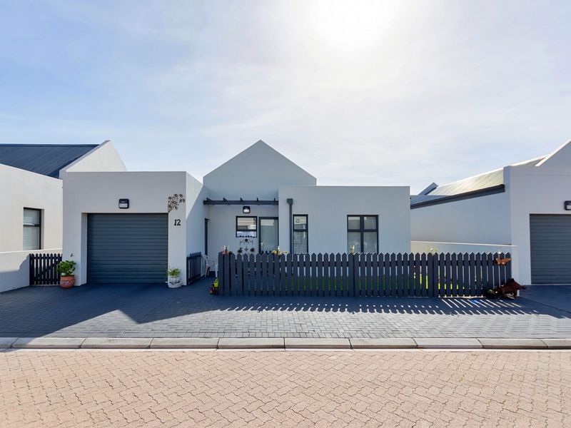 Modern single-story residential facade featuring a paved driveway, integrated single garage, and a neat picket fence entrance.