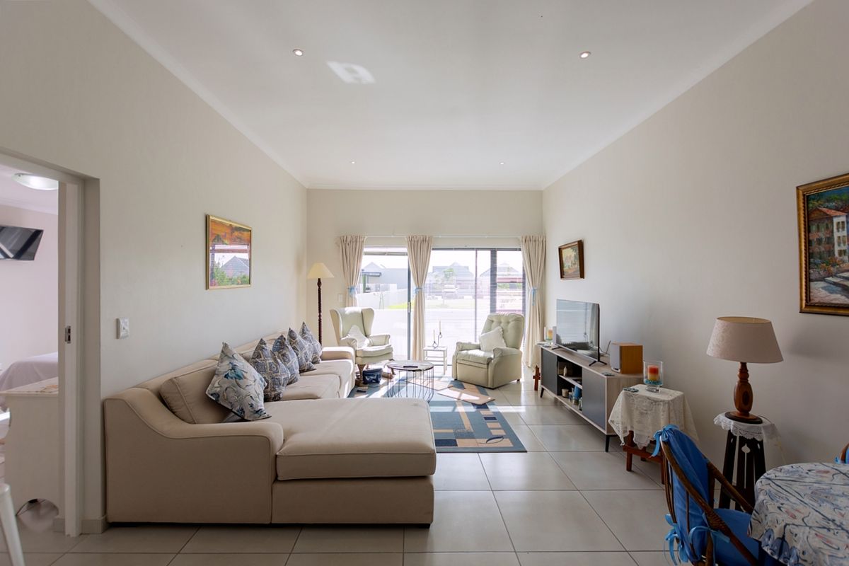 A bright and spacious living room featuring neutral tiled flooring, recessed downlighting, and large sliding glass doors that provide access to the exterior.