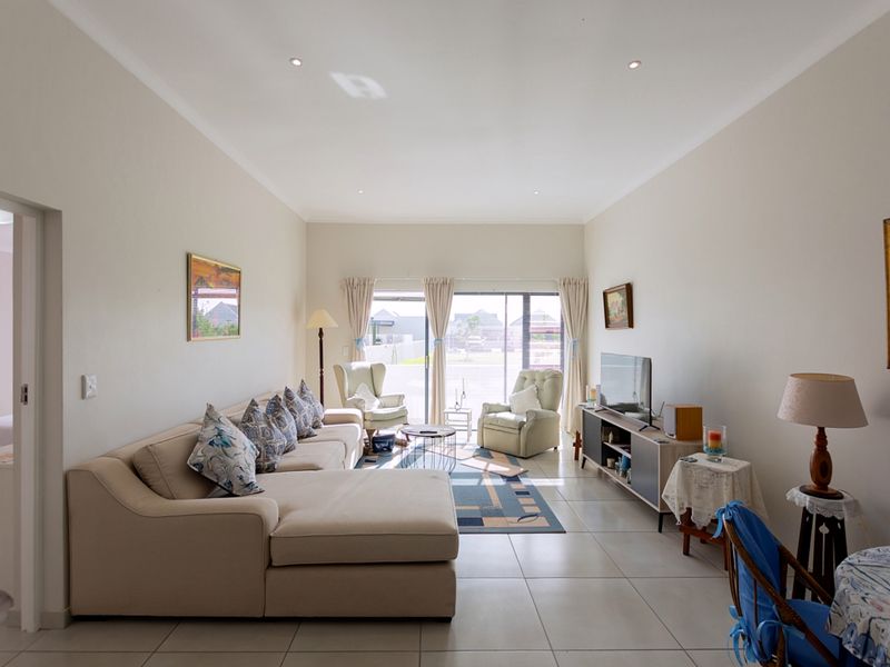 A bright and spacious living room featuring neutral tiled flooring, recessed downlighting, and large sliding glass doors that provide access to the exterior.
