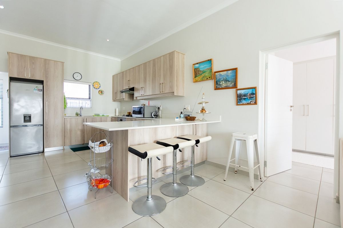 Modern kitchen featuring light wood-finish cabinetry, stone countertops, a breakfast bar, and tiled flooring, offering a clean and functional culinary space.