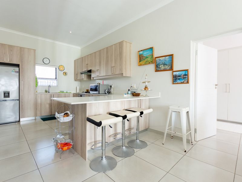 Modern kitchen featuring light wood-finish cabinetry, stone countertops, a breakfast bar, and tiled flooring, offering a clean and functional culinary space.