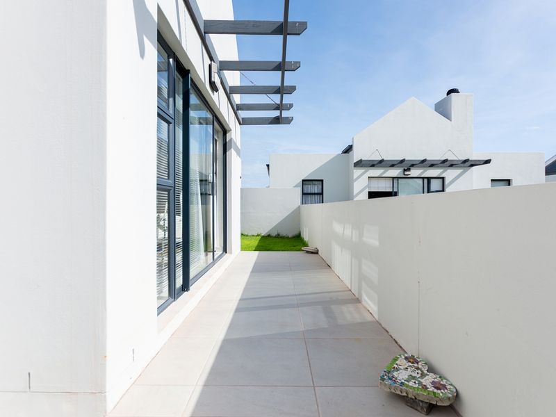 A clean, modern outdoor patio area featuring tiled flooring, a pergola structure, and large sliding glass doors leading into the home.
