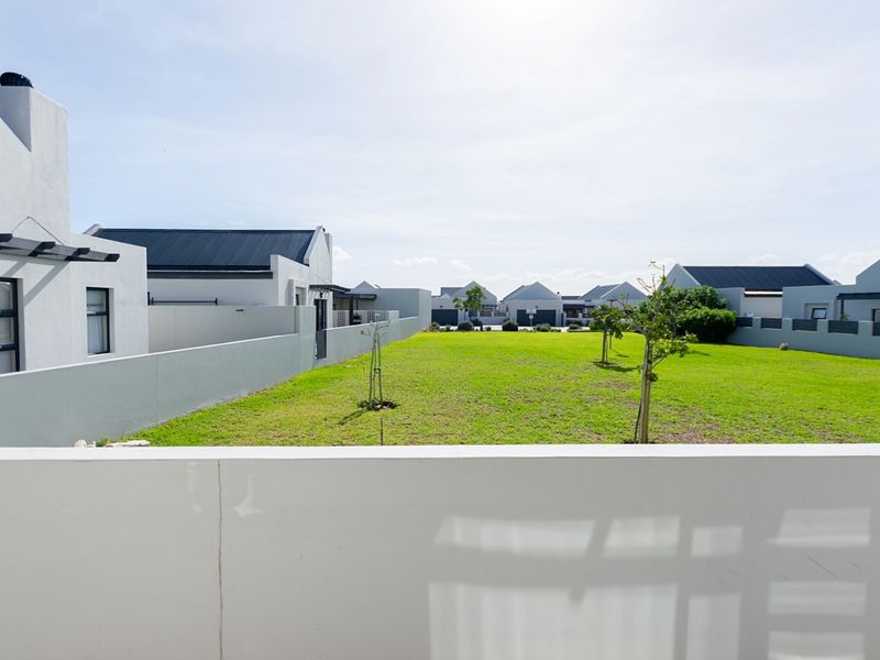 A view of the rear garden area featuring a well-maintained lawn, boundary walls, and surrounding residential properties.