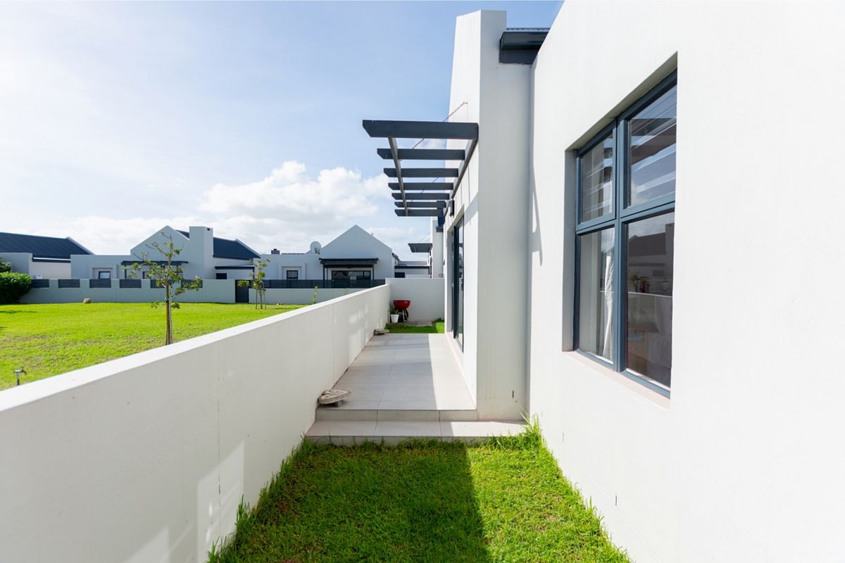 A clean rear exterior view featuring a tiled patio with a pergola, adjacent to a well-maintained lawn and boundary wall.