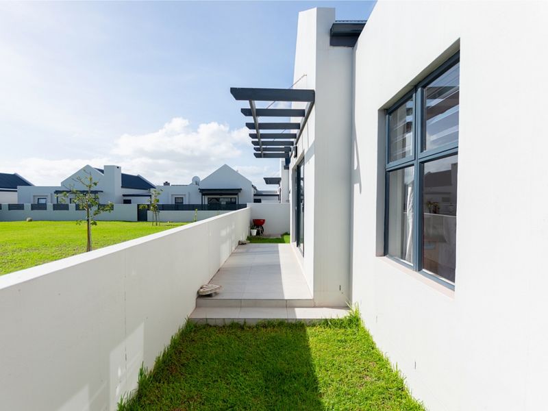 A clean rear exterior view featuring a tiled patio with a pergola, adjacent to a well-maintained lawn and boundary wall.