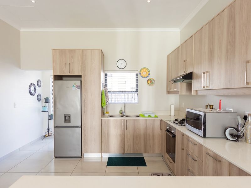 A modern kitchen featuring light-wood cabinetry, stone countertops, a built-in oven with gas hob, and tiled flooring.