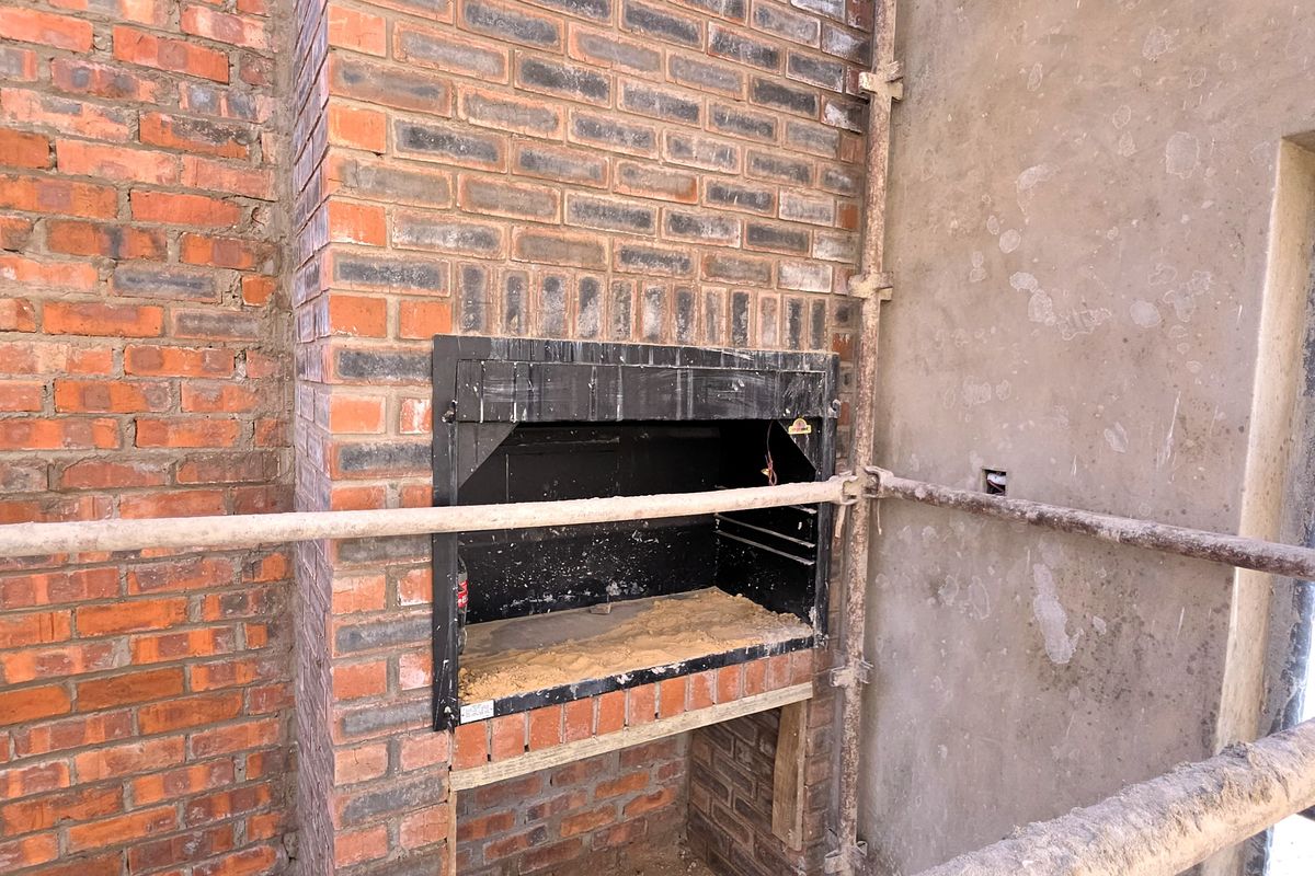 An unfinished interior space featuring a built-in brick fireplace and raw construction elements, currently undergoing renovation or building work.