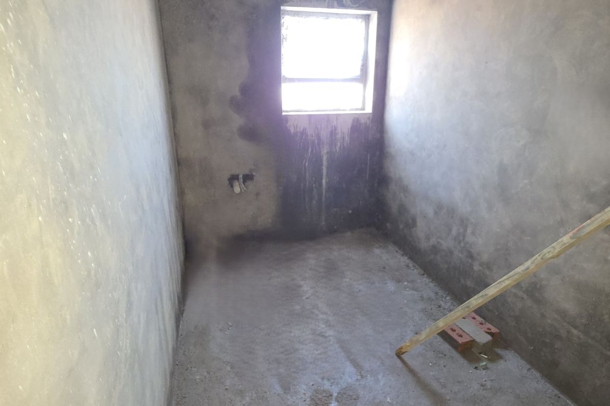 An unfinished room in shell condition featuring raw plaster walls, a concrete floor, and a single window, ready for final finishes and installation.