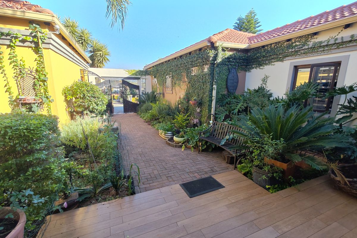 A charming rear courtyard featuring brick paving, lush climbing greenery, and a timber-look deck area connecting the home's exterior spaces.