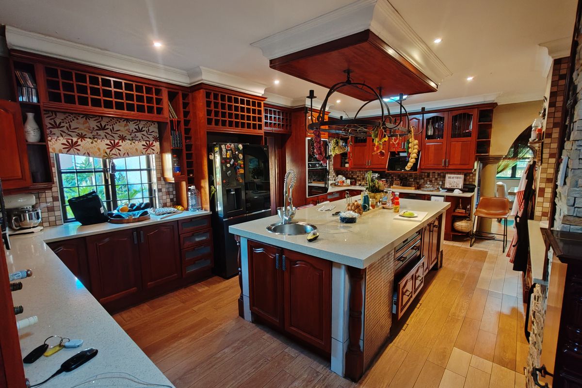 Spacious kitchen featuring rich wood cabinetry, a large central island with stone countertops, integrated appliances, and a distinctive hanging pot rack.