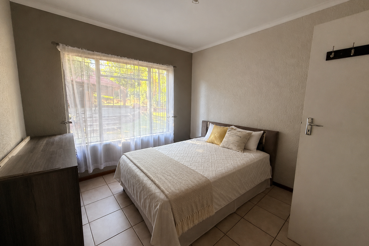 A functional bedroom featuring tiled flooring, a large window with natural light, and a neutral color palette.