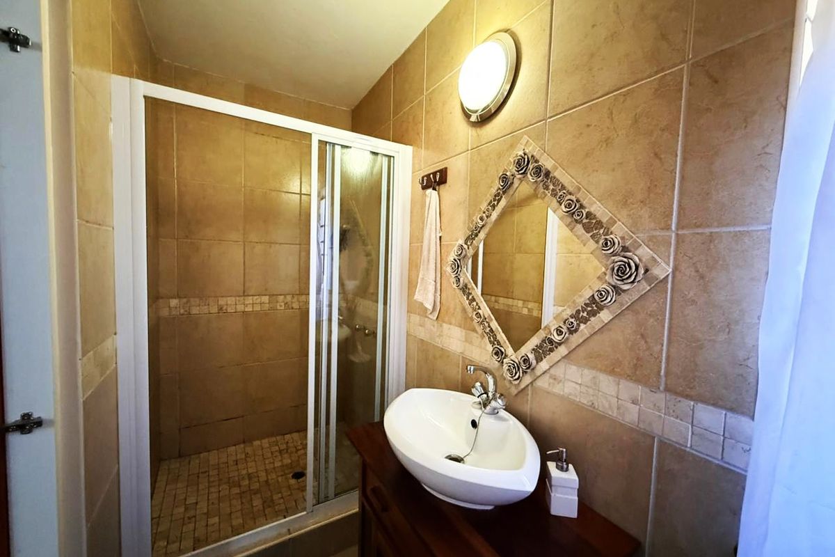 A compact bathroom featuring a walk-in shower with sliding glass doors, a vessel sink vanity, and neutral wall tiling.