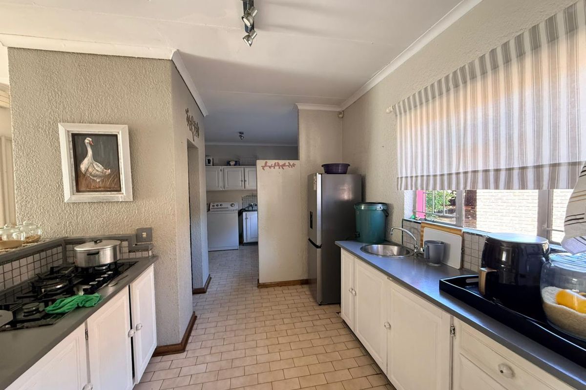 A functional kitchen featuring white cabinetry, a built-in gas hob, and a stainless steel sink, with an adjacent scullery area visible in the background.