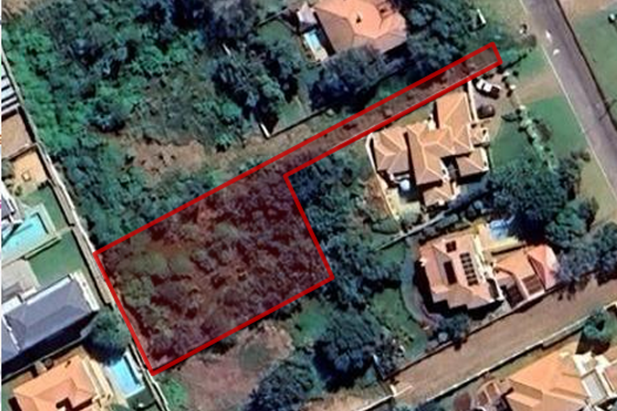 An aerial view of a vacant residential plot outlined in red, situated within an established suburban neighborhood with surrounding homes and mature vegetation.