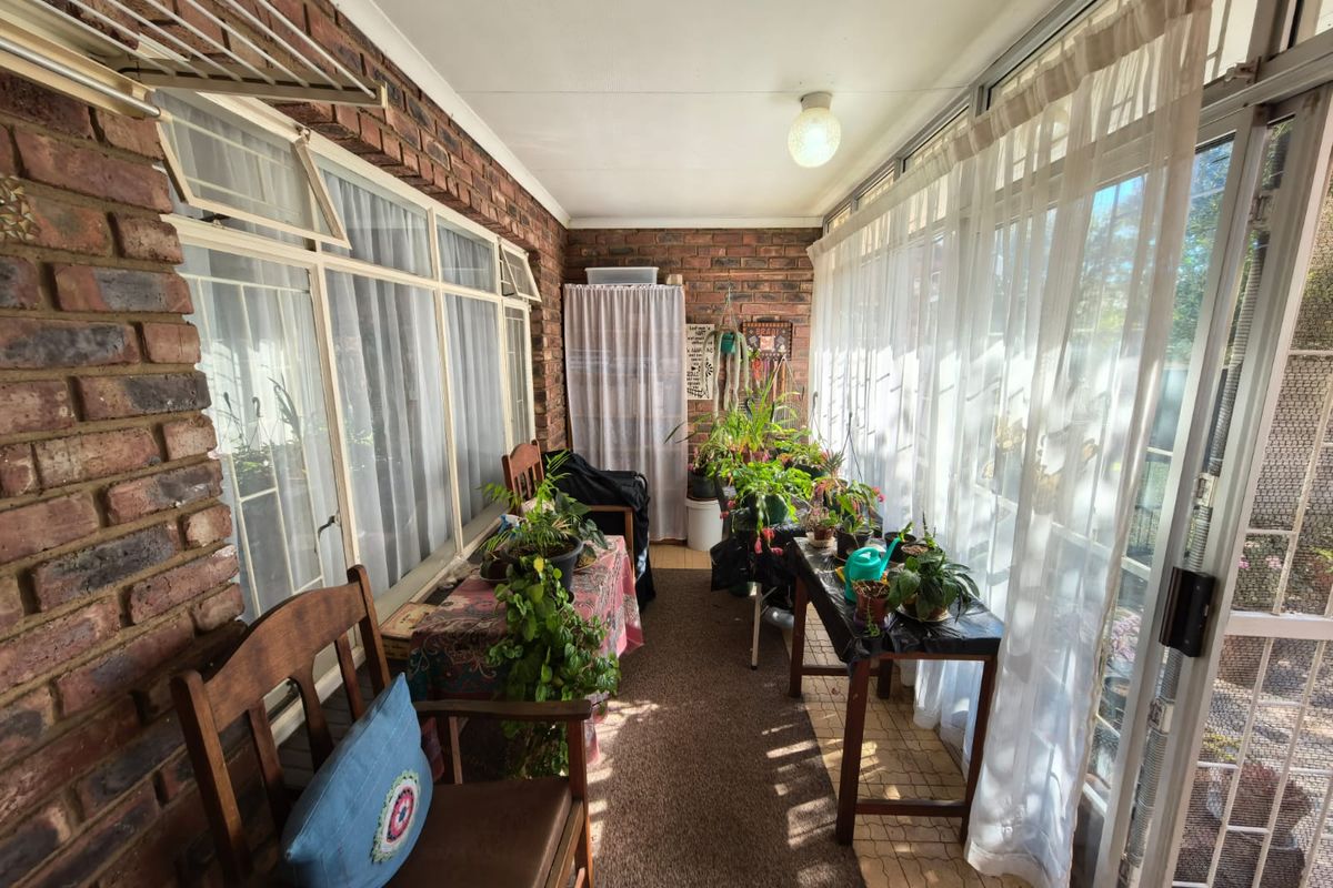 A sun-drenched enclosed patio featuring exposed brick walls, large sliding glass doors, and tiled flooring, offering a versatile space for relaxation or indoor gardening.