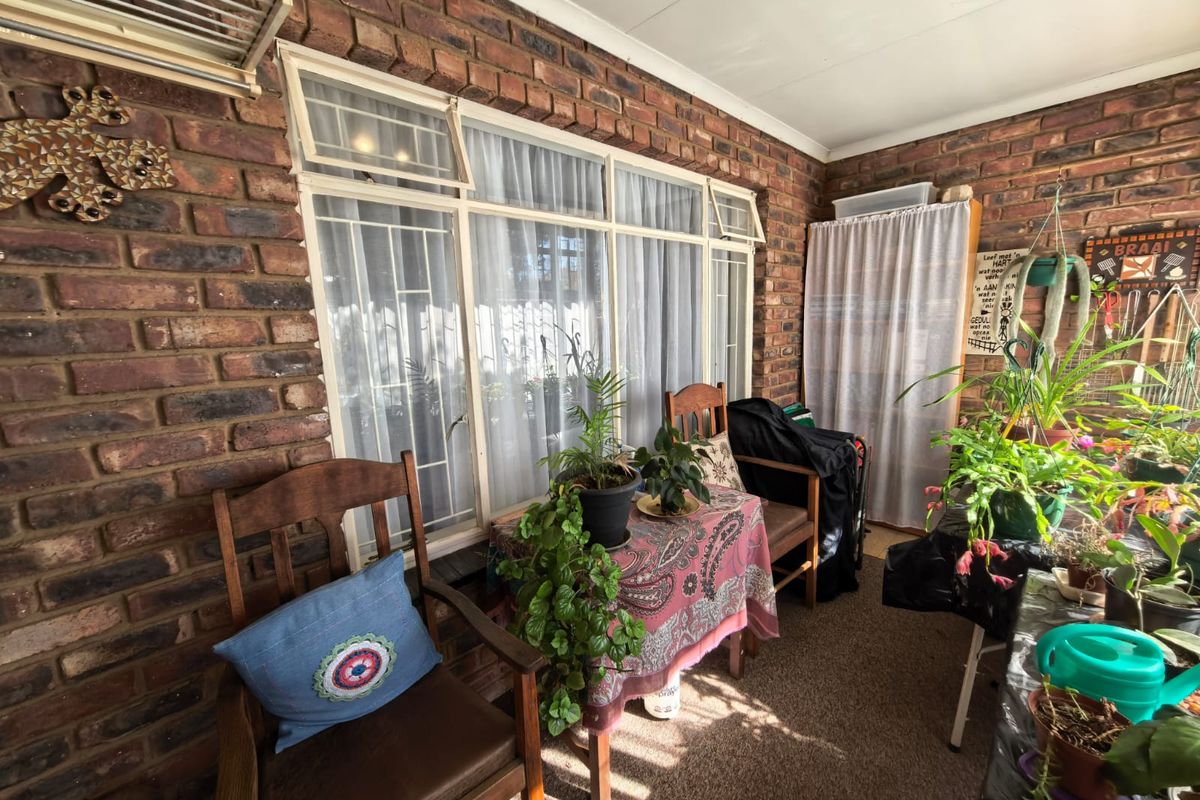 A covered patio area featuring exposed brick walls and large windows with security bars, providing a functional outdoor living space.