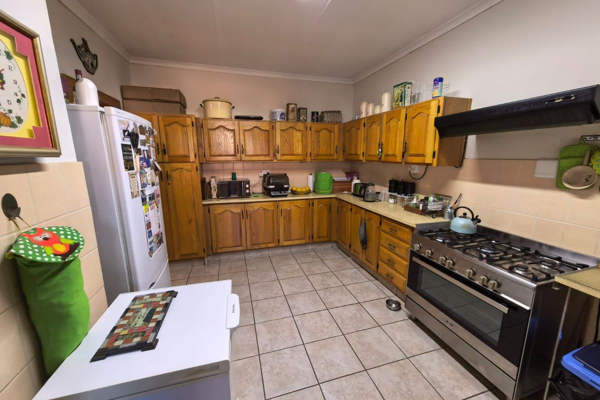 A functional kitchen featuring wooden cabinetry, tiled flooring, a gas stove with an extractor fan, and tiled backsplash throughout the workspace.