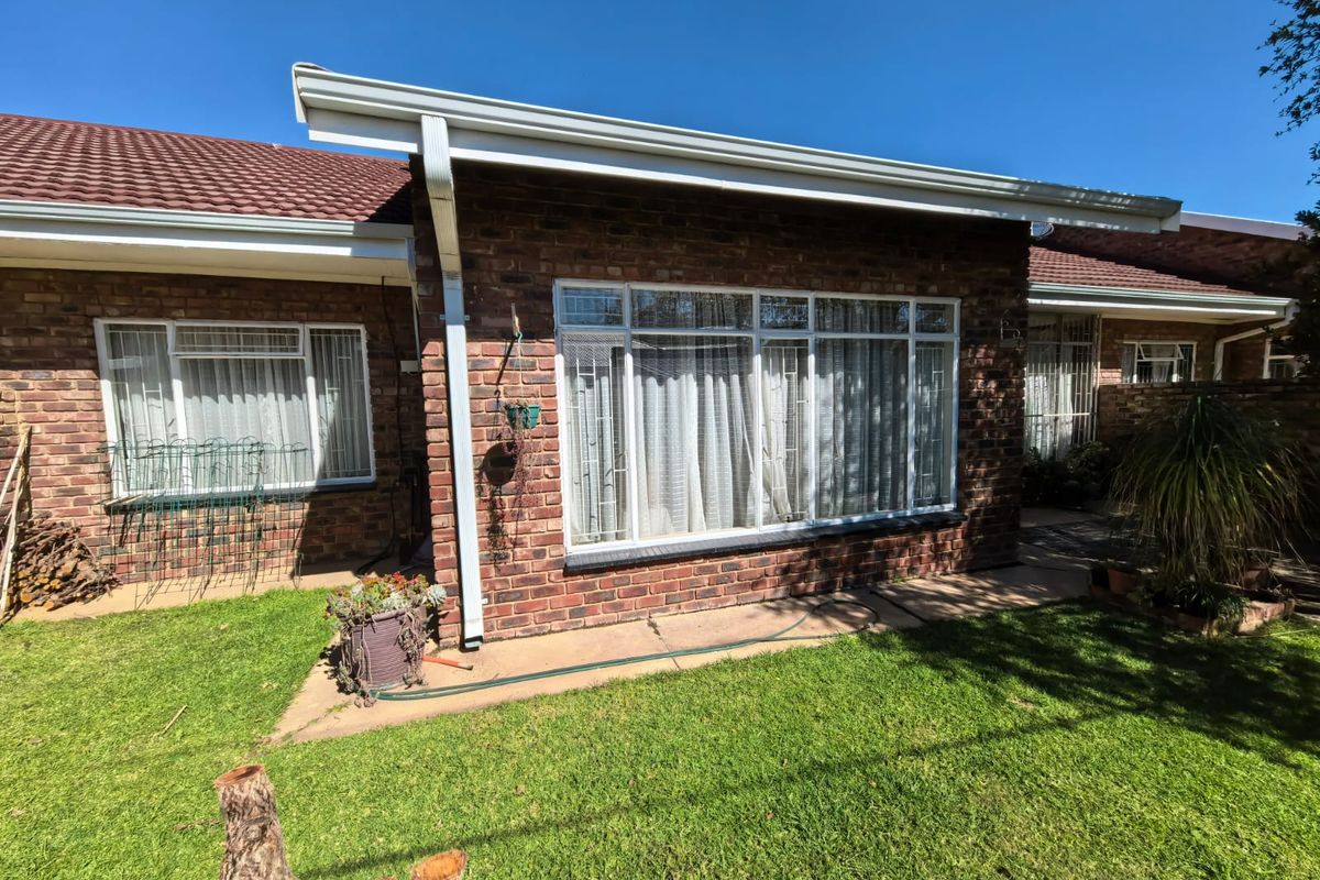 Rear view of a face brick townhouse featuring a tiled roof, paved walkway, and secure aluminium-framed windows overlooking a small garden area.