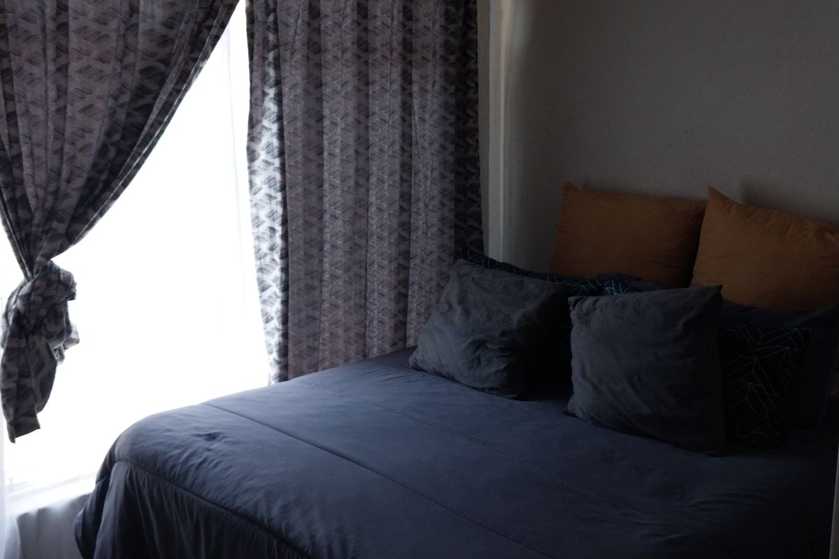 A bedroom featuring laminate flooring and cove cornice detailing, with natural light entering through a window covered by curtains.