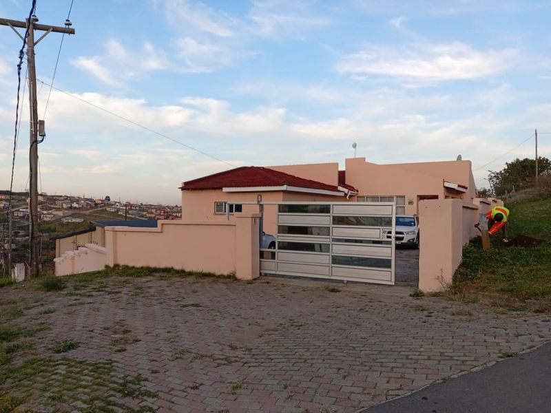 Front view of a residential property featuring a paved driveway, perimeter wall, and a modern sliding gate with a tiled roof structure.