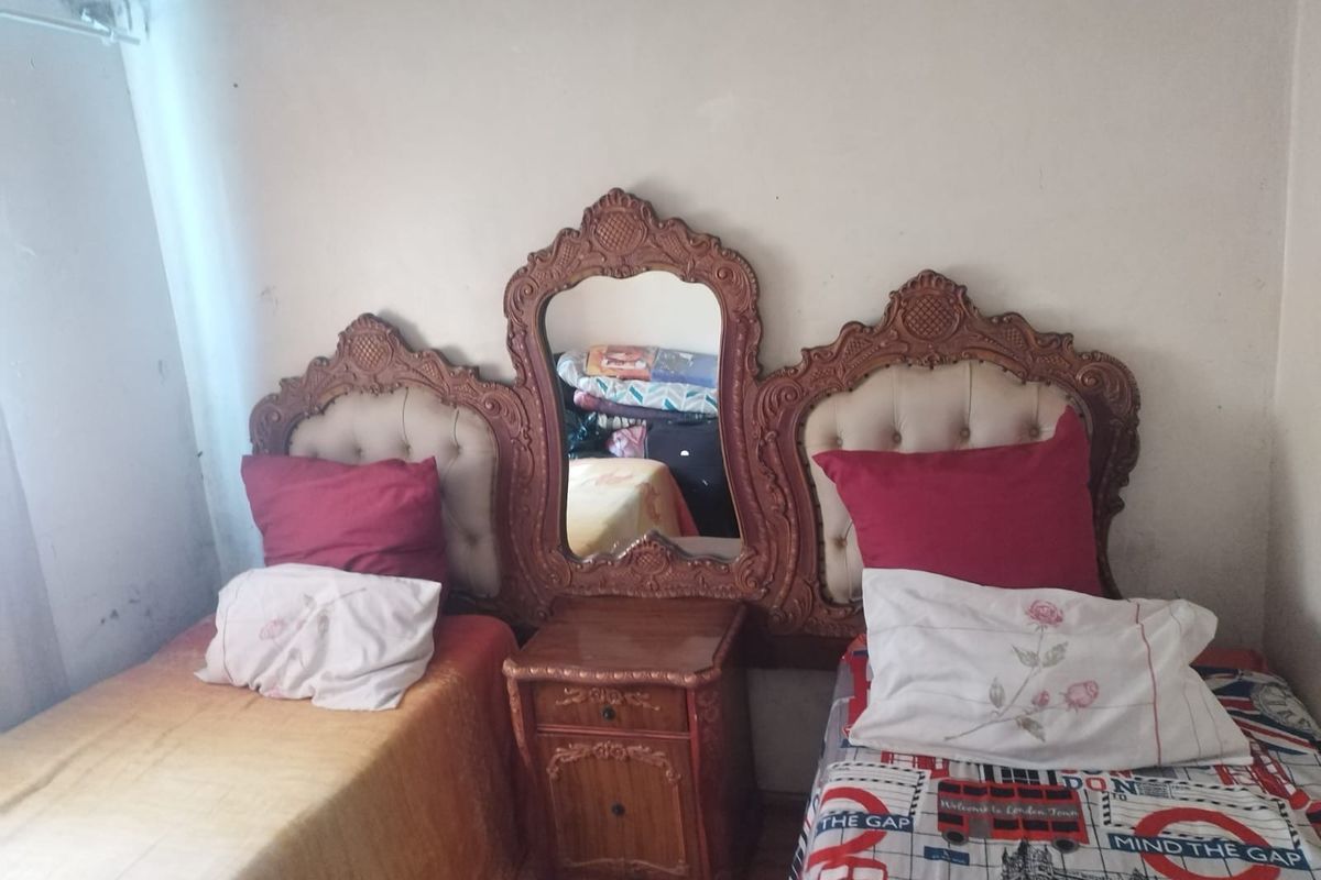 A bedroom featuring a central built-in wooden headboard and vanity unit with an integrated mirror between two bed spaces.